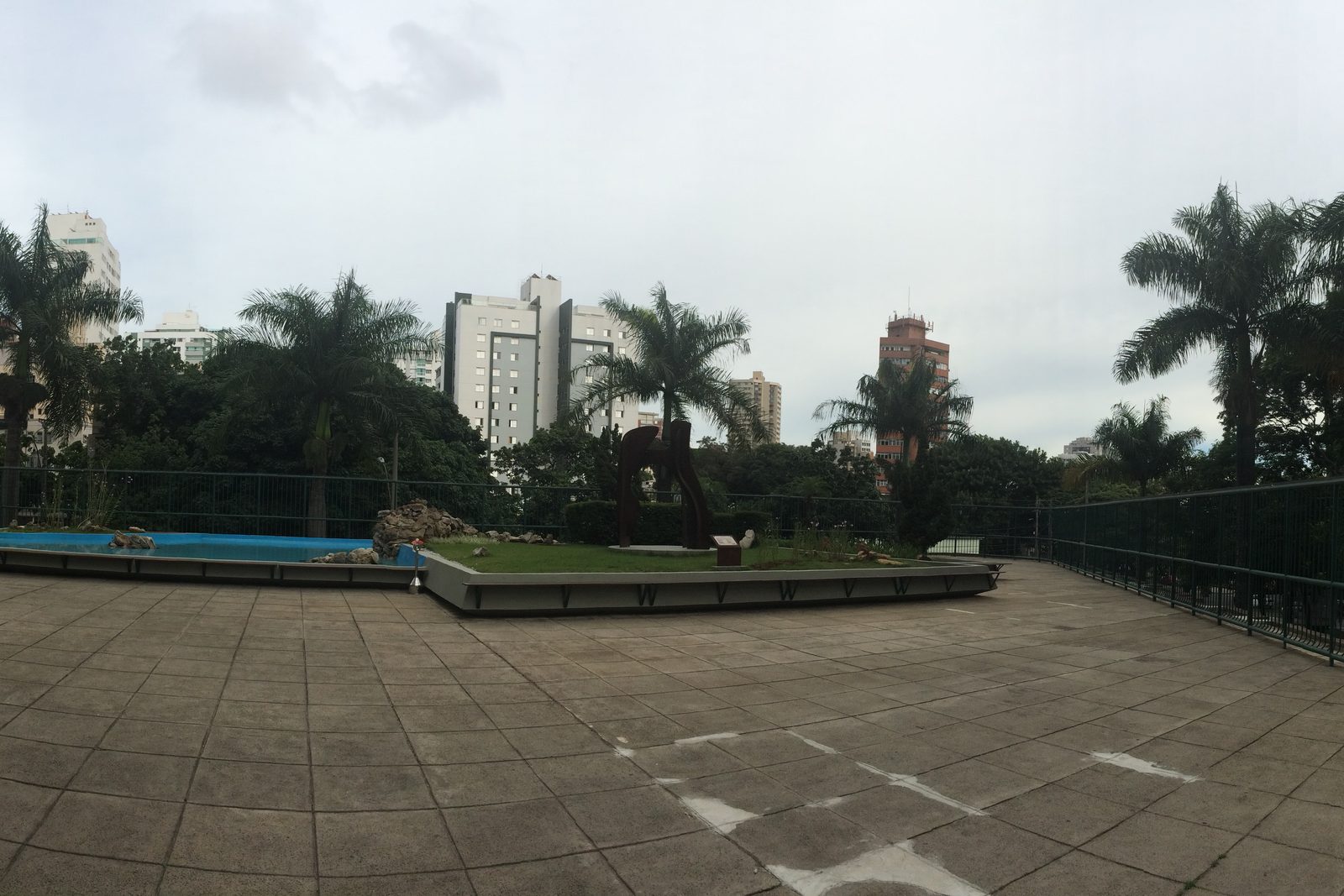 Fotografia panorâmica. Edifício corporativo horizontal de vários andares, com fachada de concreto e faixas de janelas, ocupando um quarteirão em avenida arborizada de Belo Horizonte.