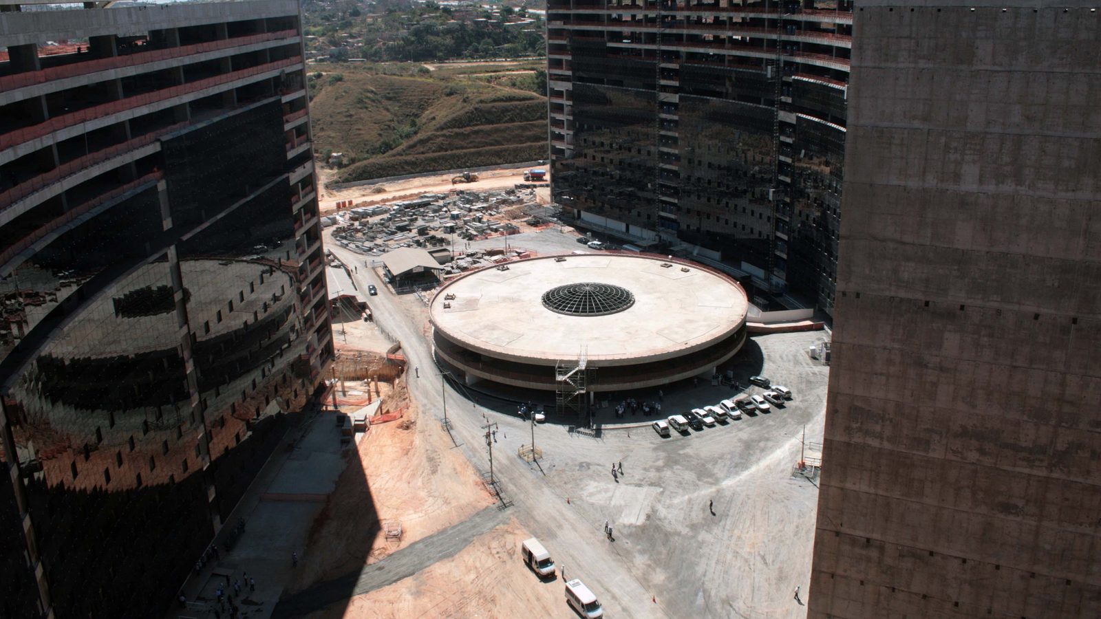 Fotografia. Os dois blocos suspensos da Cidade Administrativa de Minas Gerais, sede do governo estadual, vistos de fora, com o espelho d'água à frente.