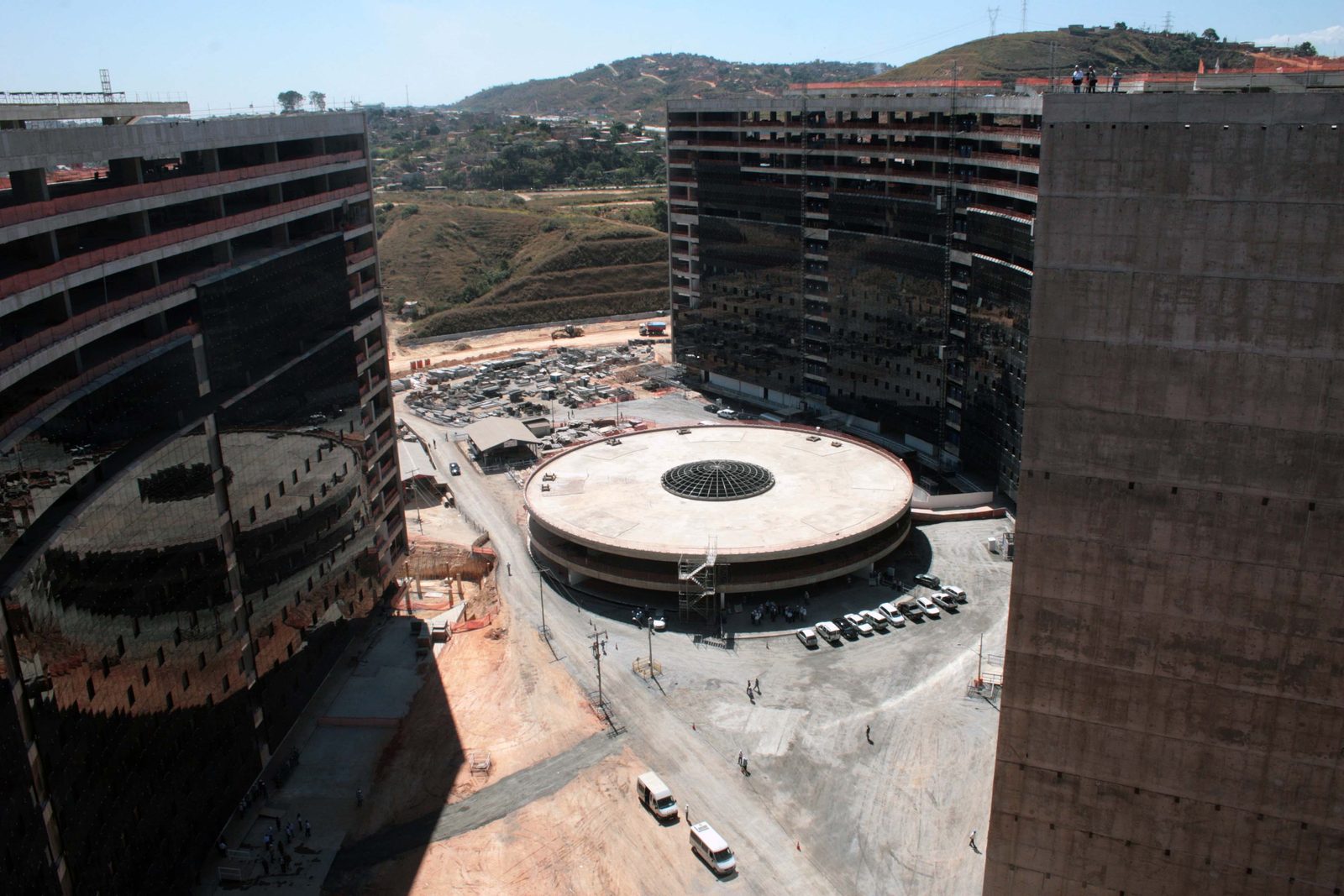 Fotografia. Os dois blocos suspensos da Cidade Administrativa de Minas Gerais, sede do governo estadual, vistos de fora, com o espelho d'água à frente.