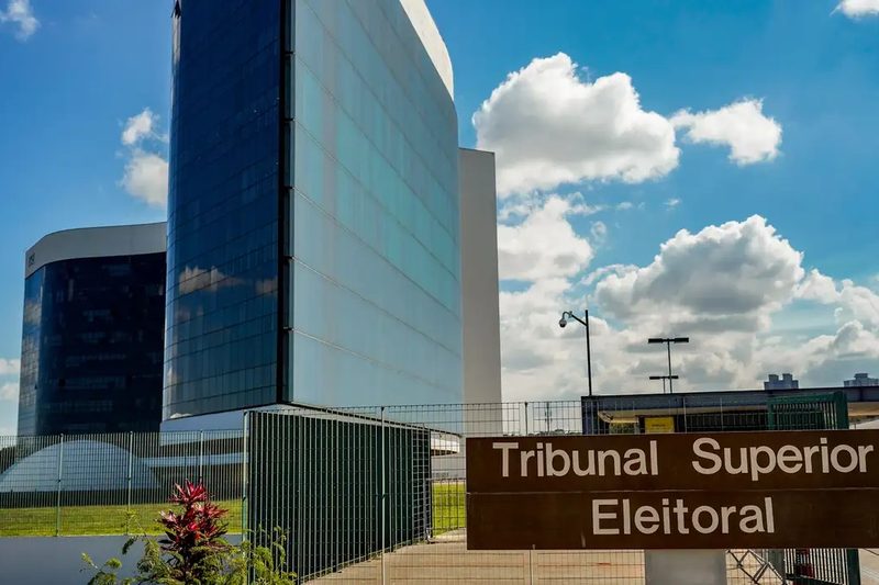 Fotografia. Plenário do Tribunal Superior Eleitoral, com a bancada dos ministros ao fundo e o brasão da República ao centro.